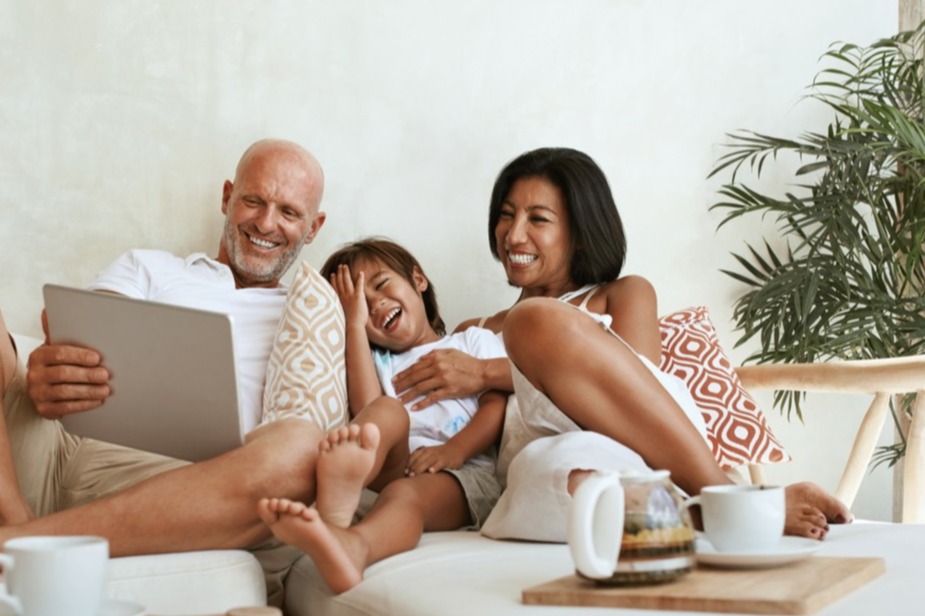family with one daughter sitting in the middle smiling on the couch