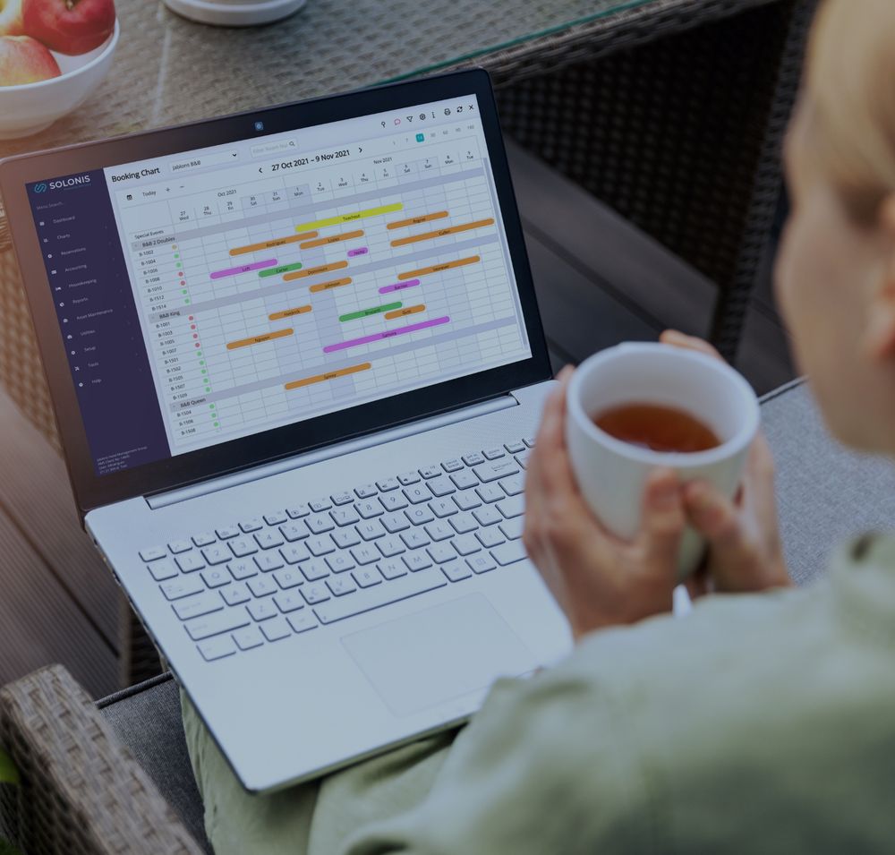 picture of a blonde hotel woman employee holding cup of coffee looking at latptop with a colorful spreadsheet on the screen